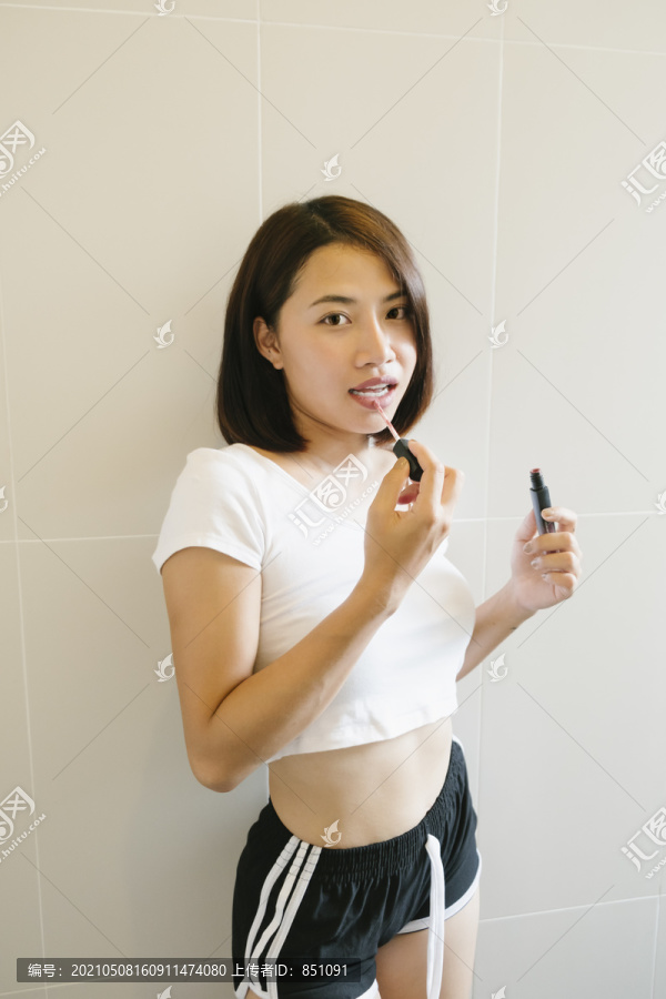 性感的亚洲泰国女人穿着白色衬衫和黑色裤子，涂上白色背景的唇膏。垂直射击。