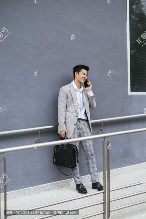 穿着正装的聪明亚泰商人在户外打电话，手里拿着黑包。