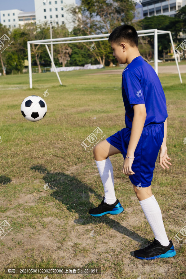 穿着蓝色足球服的男孩在田里踢足球的肖像。