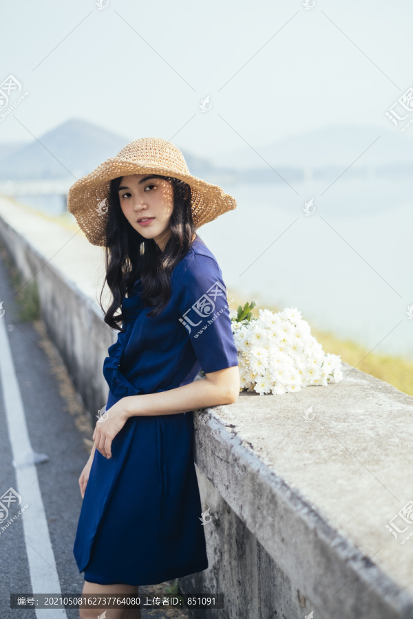 穿着深蓝色连衣裙的漂亮女孩，靠在坝上，身上开着白花。