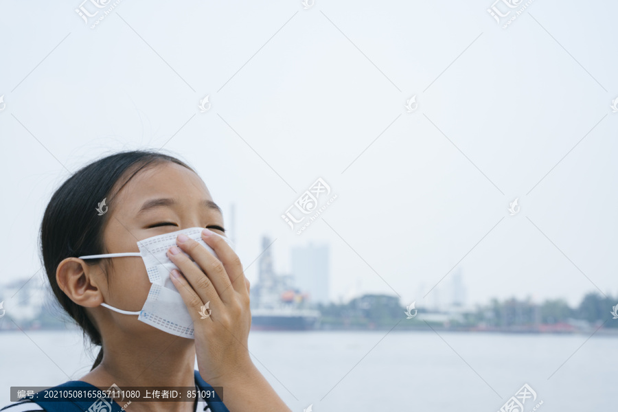 病毒防护概念-戴着防护面具的亚洲小女孩，在雾霾天站在河边。到处都是污染。用手捂住嘴。