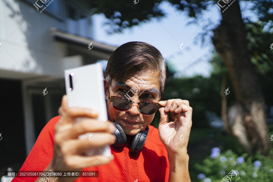 穿红色t恤的老人抓起太阳镜，惊奇地看着智能手机。