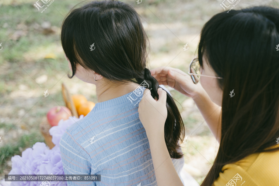 黄色t恤女孩在野餐时为蓝色t恤女孩做发型设计。