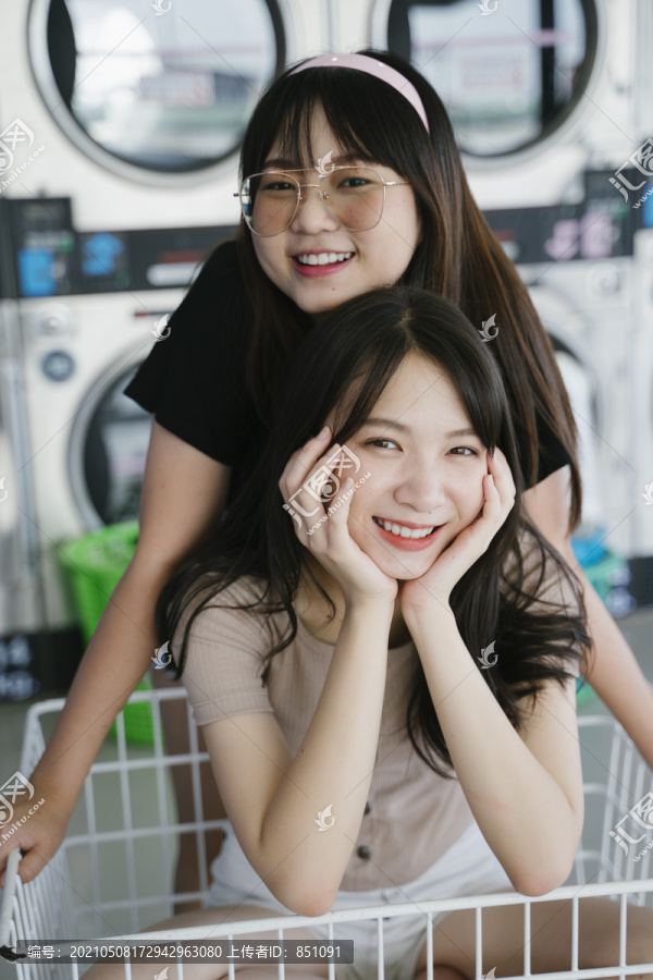 两个女孩在自助洗衣店一起玩着篮子手推车。