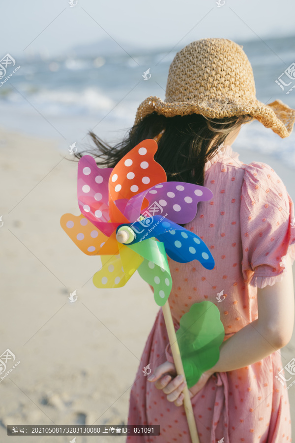 可爱的女孩站在沙滩上，身后是五颜六色的风车。