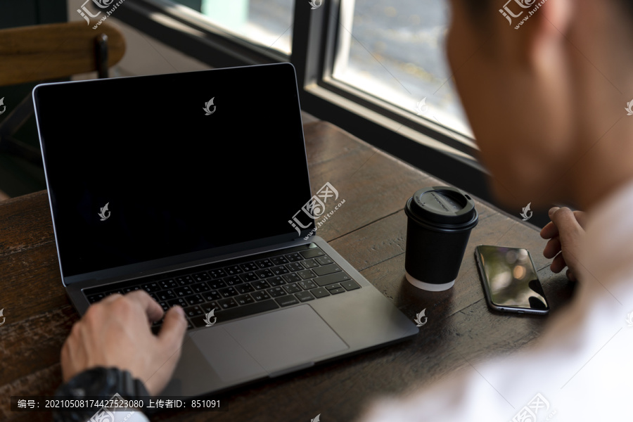 商人在咖啡馆用笔记本电脑工作，桌上放着咖啡杯-复印空间。