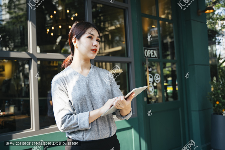 美丽的亚洲年轻女子在街上的咖啡馆背景上使用平板电脑。