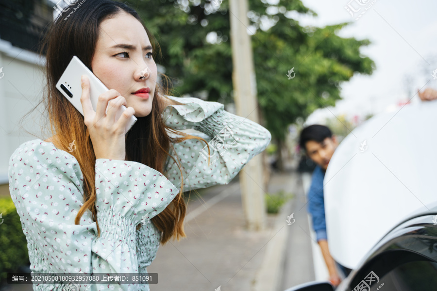 愤怒的亚洲女人开始用电话打电话给机械师来这里修车。年轻女子一边用手机一边看着街上抛锚的汽车。