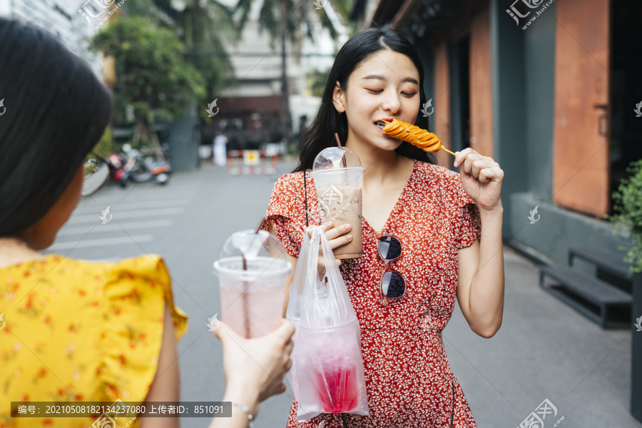 穿着红裙子的亚洲美女和穿着黄裙子的朋友一起吃街边小吃。