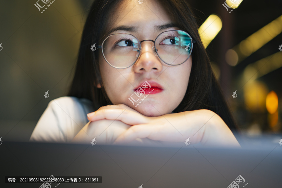特写镜头：年轻漂亮的亚洲女人戴着眼镜，晚上在笔记本电脑前工作。