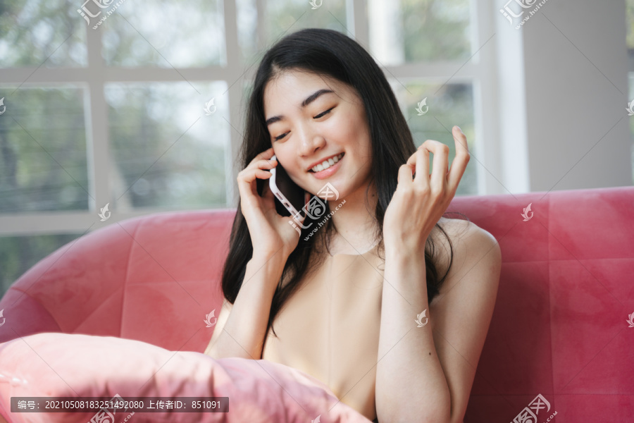 长发女孩坐在粉色沙发上，微笑着给男友打电话。