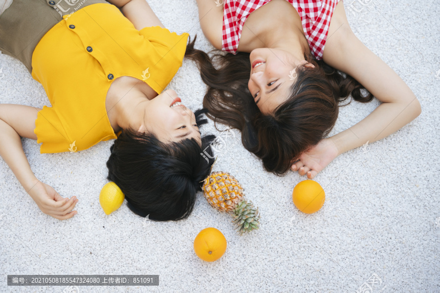 两位亚洲女性密友暑假躺在地上。热带水果。顶视图。穿黄衬衫和红衬衫的亚洲女人。旅游度假。假日周末。