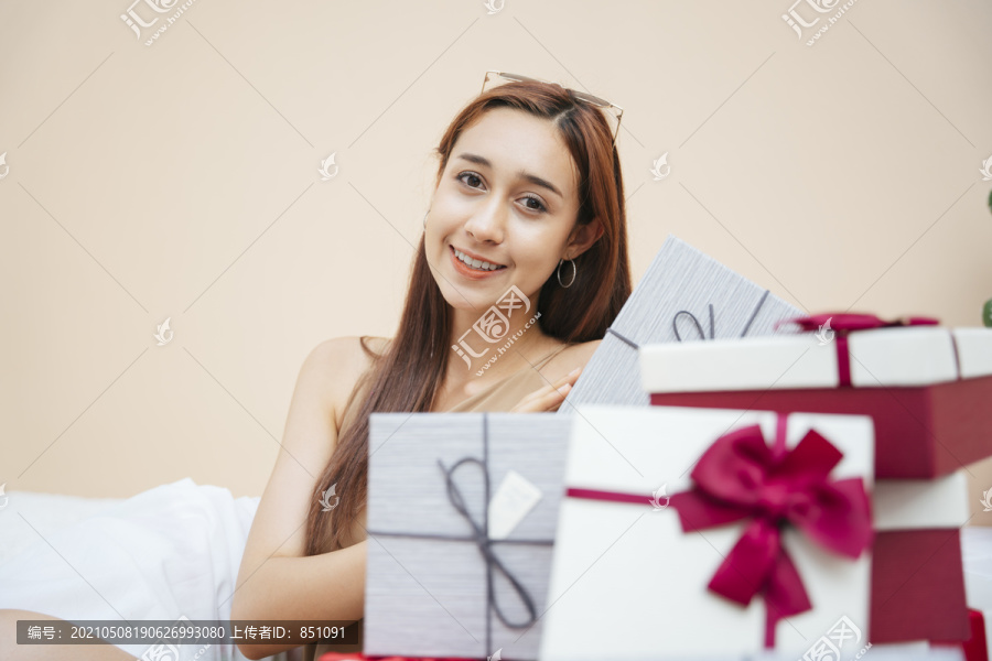 坐在一堆礼物盒里的美女。快乐的脸和自信的微笑。以米色奶油色为背景。