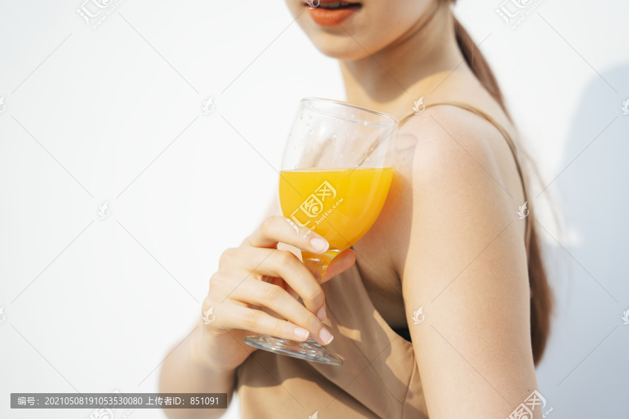 在白色背景下，一个漂亮的黑发女人在玻璃杯中喝橙汁。