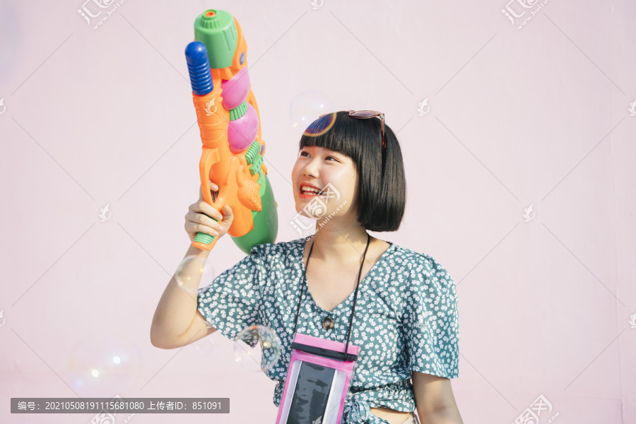 美丽的短发女子用水枪欣赏泰国泼水节。快乐和幸福。现代泼妇。在粉红色背景上孤立。曼谷的泼水节。