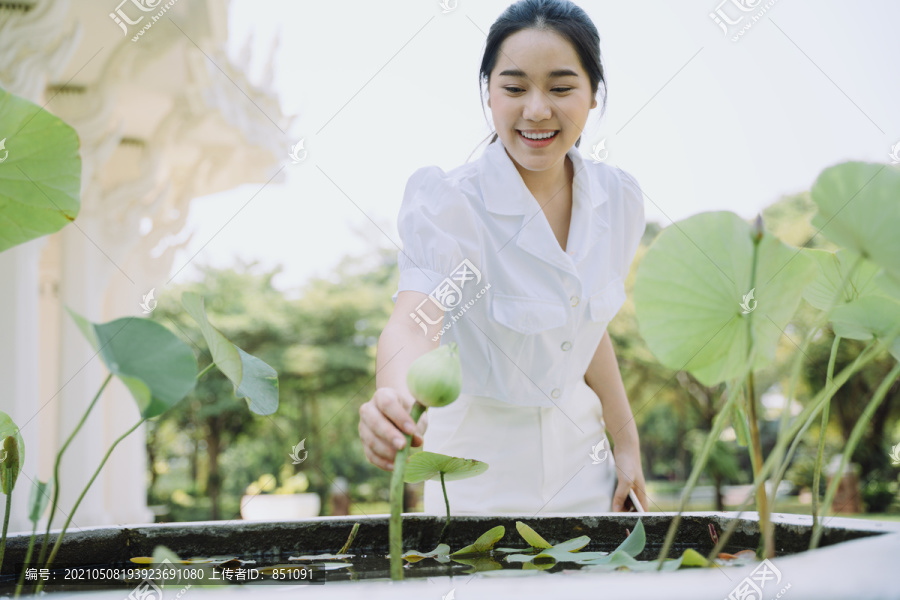 身穿白衬衫的黑马尾女子弯腰抓住庙里盆里的白莲花。