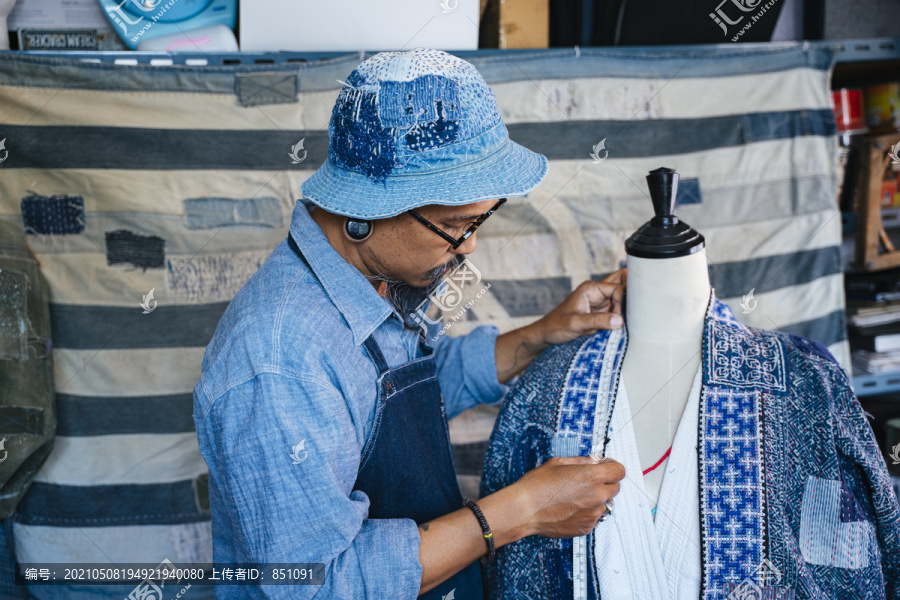 一个穿着蓝色衬衫和围裙的男人在人体模型上测量衣服以使其合身，测量衣领。