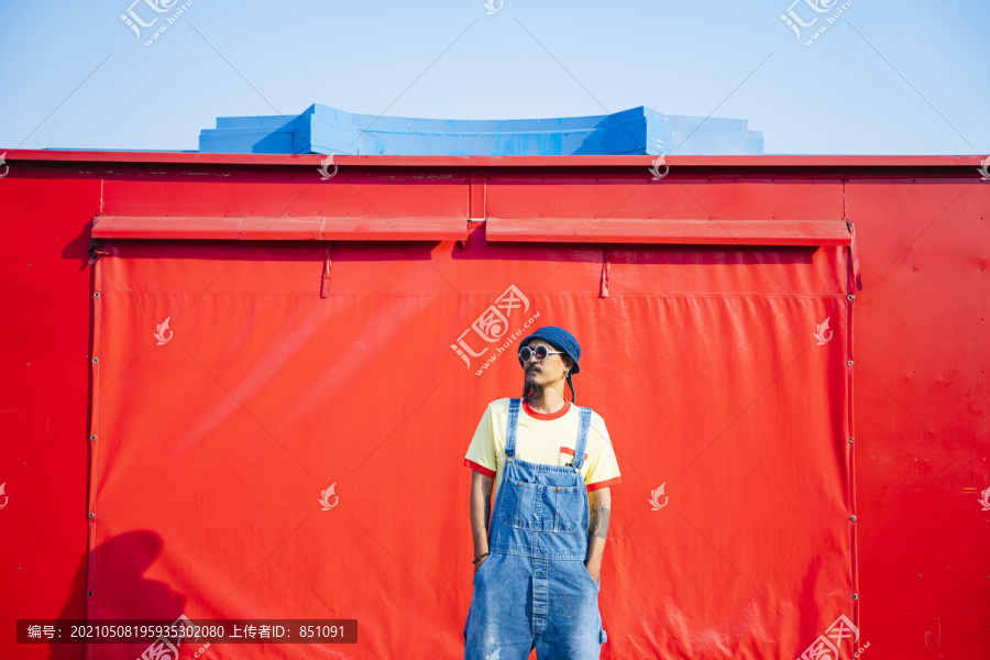 一名身穿黄色t恤和牛仔工作服的男子站在红色拖车前踢腿。
