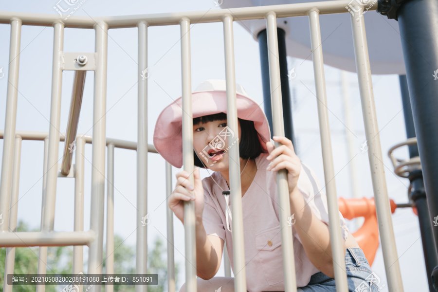 美丽的亚洲女人戴着帽子在操场上玩耍，坐在笼子后面。