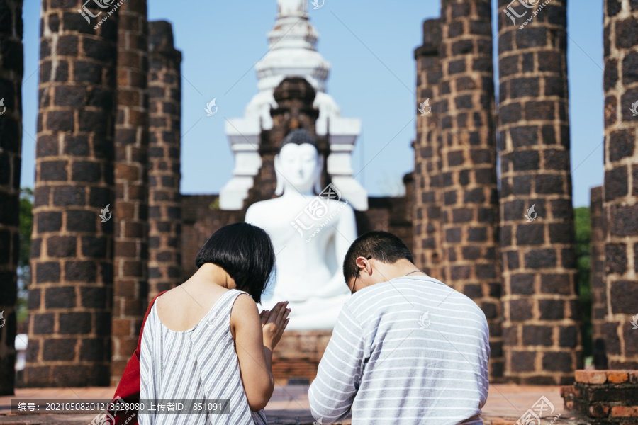 观光客夫妇的后景是对他们面前的白色大佛的尊敬和崇拜。这对夫妇鞠躬敬拜这尊巨大的佛像。