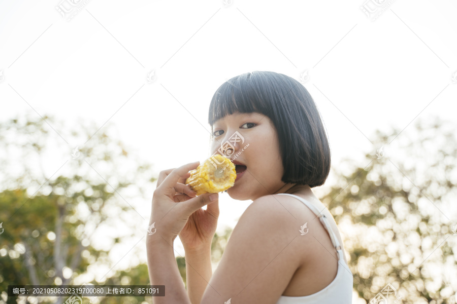 特写亚洲女人鲍勃发型吃煮玉米户外。健康的水果和蔬菜。