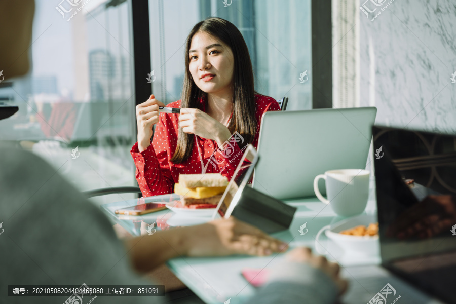 身着红衫的美丽年轻的亚泰女商人在会议室与同事做报告。漂亮的老板女商人。