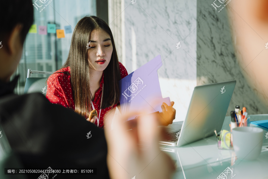 穿着红衬衫的美丽年轻的亚泰女商人正在解释热腾腾的商业工作阅读紫色文件夹内的文件纸。会议室。