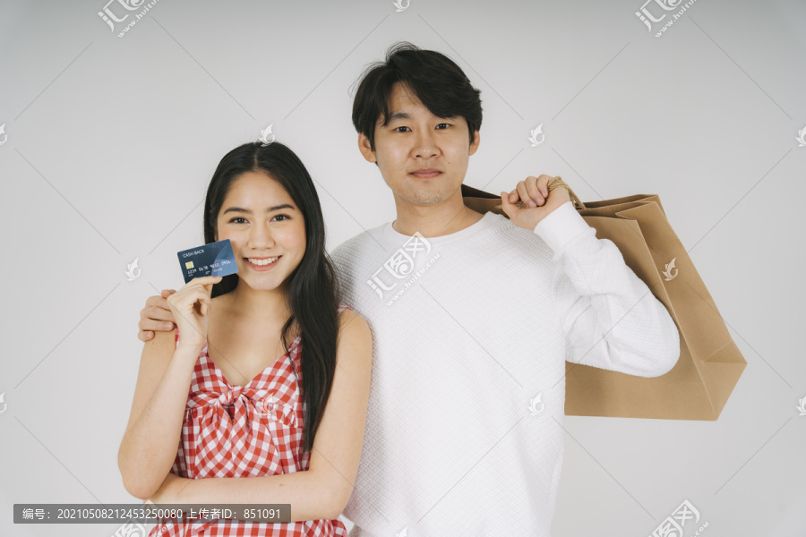 一对夫妇一起去购物，一个男人在商场里为一个女人拿购物袋。女人拿着信用卡，男人拿着购物袋。