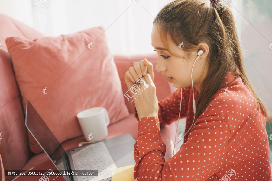 在家工作的概念-穿着红色睡衣衬衫的漂亮年轻女子用耳机和同事在笔记本电脑上交谈。检疫。