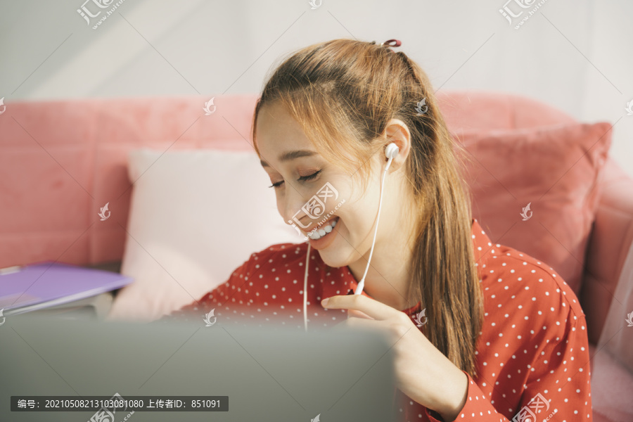 在家工作的概念-穿着红色睡衣衬衫的美丽年轻女子在笔记本电脑上与同事交谈。在家工作。使用耳机。检疫。
