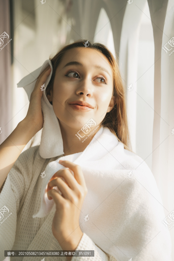 性感的年轻女子穿着白色浴衣用毛巾擦干净头发后走出浴室。室内的。公寓。