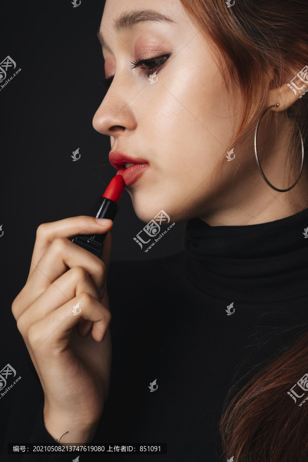 在黑暗的背景下，穿着黑色毛衣的漂亮年轻女子的特写肖像。女人用红色唇膏。化妆品概念。