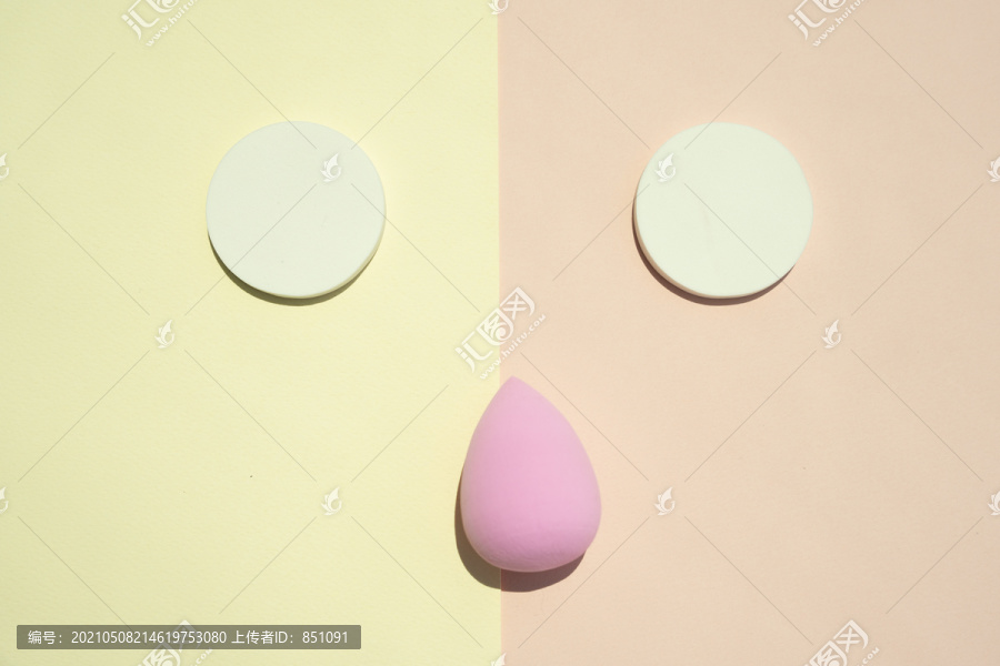 化妆工具化妆品。粉扑隔离在两个色调的颜色黄色和粉红色。一张滑稽的脸。
