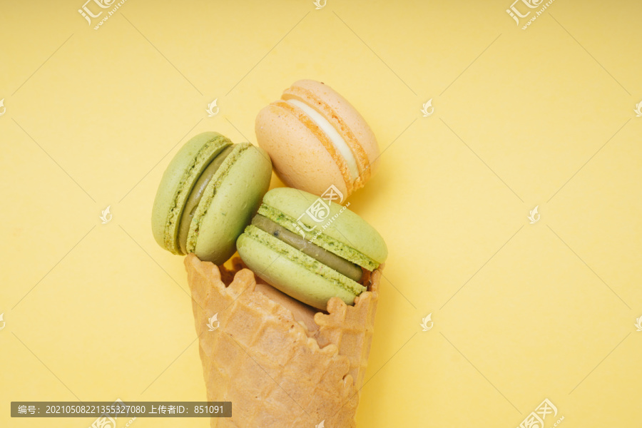 黄色背景上的华夫饼干冰淇淋筒上有一套橙色和绿色的美味麦卡龙。法式蛋糕。