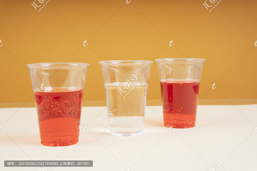 两个红色苏打水和淡水的塑料杯，一个在橙色背景上。