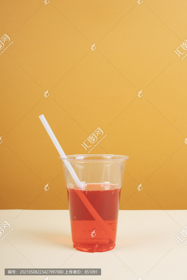 桌上放着吸管的塑料杯里的红色起泡水。