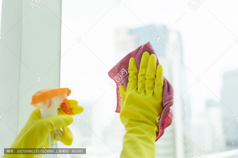 女佣手戴黄色手套，用清洁剂喷雾瓶和架子布清洁玻璃镜。打扫房间。Covid-19冠状病毒预防。