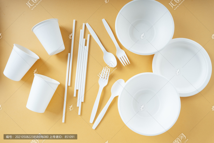 一次性塑料杯，叉子，勺子，碗，平底锅和稻草在橙色的背景。