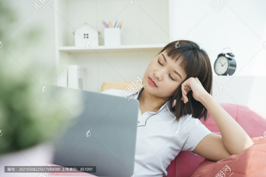 泰国亚裔大学生在家学习时戴着耳机在笔记本电脑前。在Covid-19爆发期间呆在家里。她睡在中产阶级区