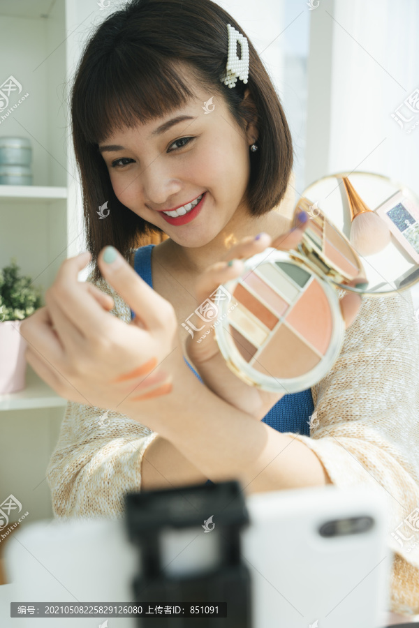 美丽年轻的亚洲美女博客评论化妆品产品与智能手机的实时流。在线影响力女孩社交媒体营销现场热气腾腾的智能