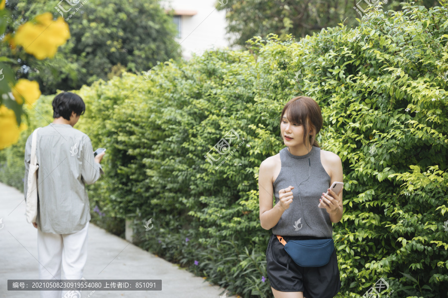 亚泰女子在公园慢跑，看着智能手机上的音乐播放列表，从男子身边走过。