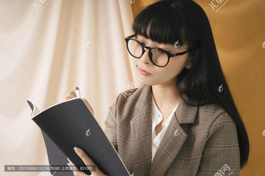 美丽的女商人戴着眼镜和西装外套，看着一本书上的报告。漂亮的书呆子女人读着一本书，带着深思熟虑的表情。