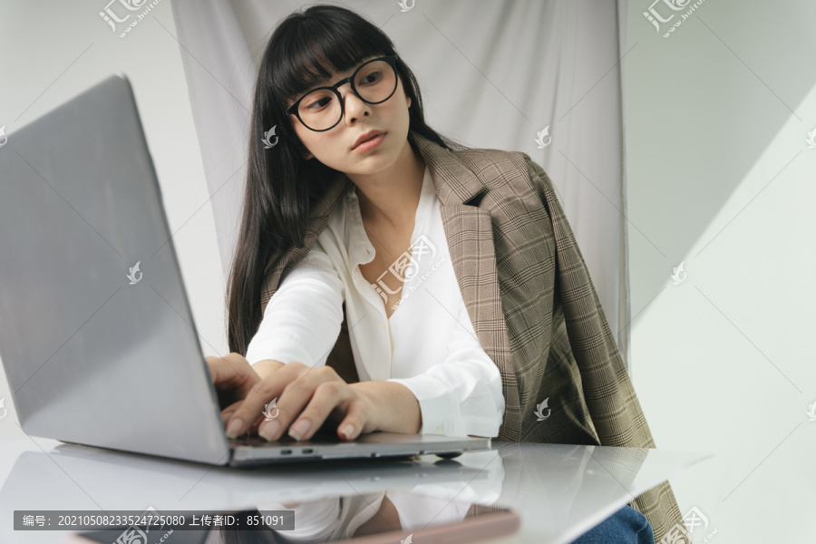 美丽的亚泰长黑发女子戴着眼镜用笔记本电脑。在家工作。