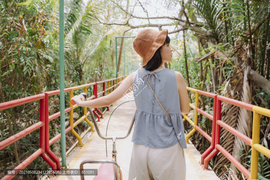 后视图-年轻的亚泰妇女骑着自行车在乡村公路上旅行。本地旅行。