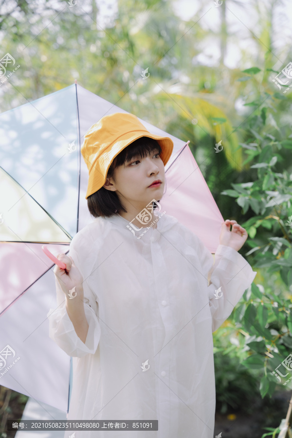 时尚写真——美丽的亚泰女人深色短发，穿着白色外套，戴黄色帽子，在雨季撑着柔和的彩虹伞。
