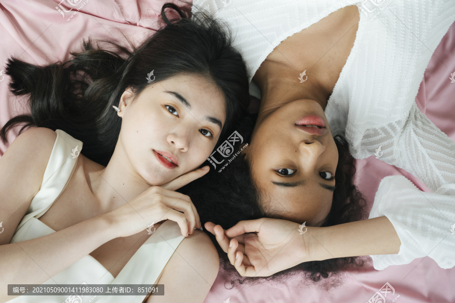 顶视图-亚洲和非洲妇女穿着白色衬衫躺在粉红色的布。