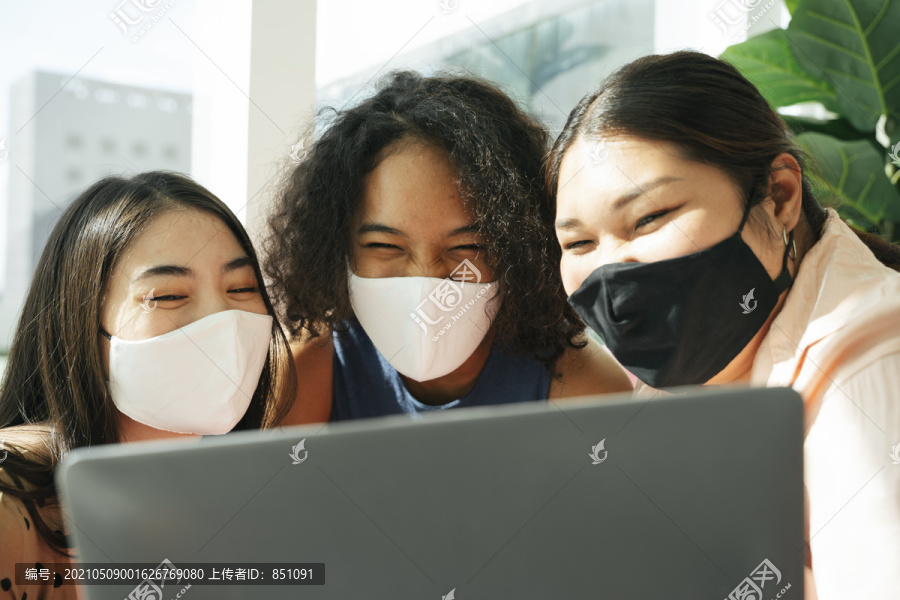 多元化社会理念。亚非妇女戴着口罩和笔记本电脑一起做视频直播。