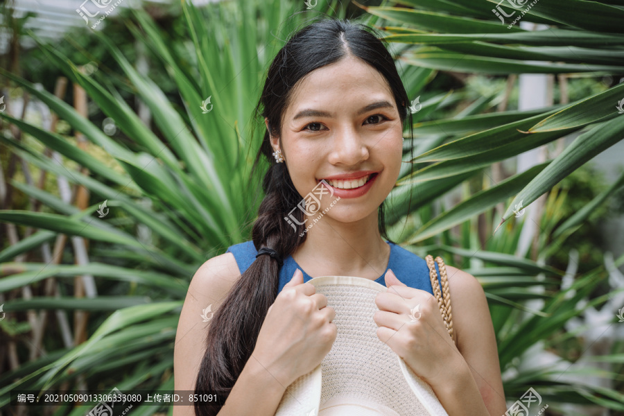 特写肖像-愉快的微笑亚洲妇女长深色头发拿着大帽子在自然背景。