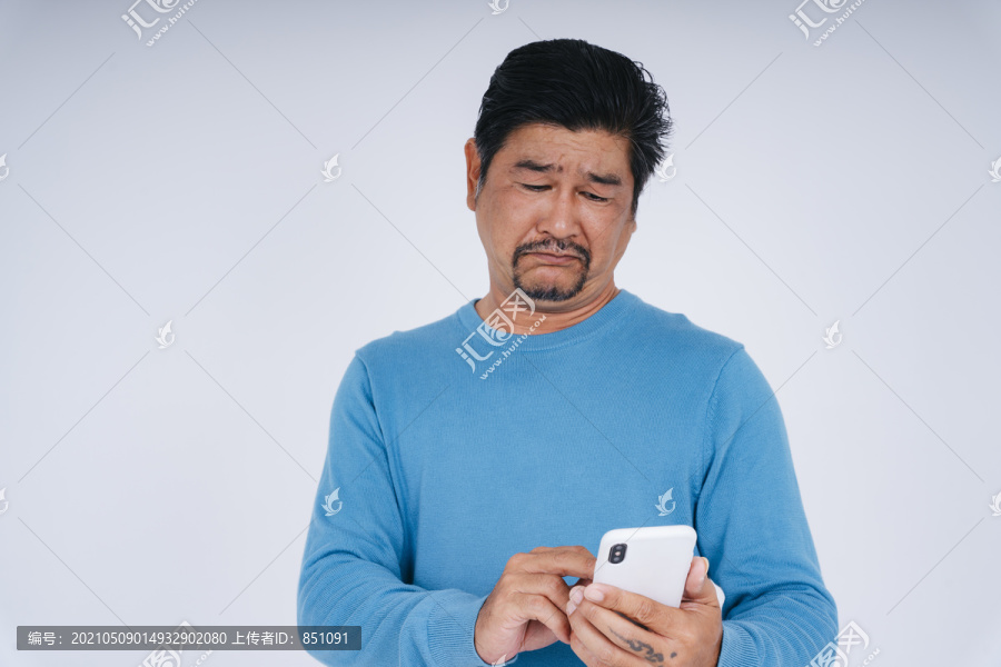 穿着蓝色长袖衬衫的老人用智能手机的画像，表情沮丧。