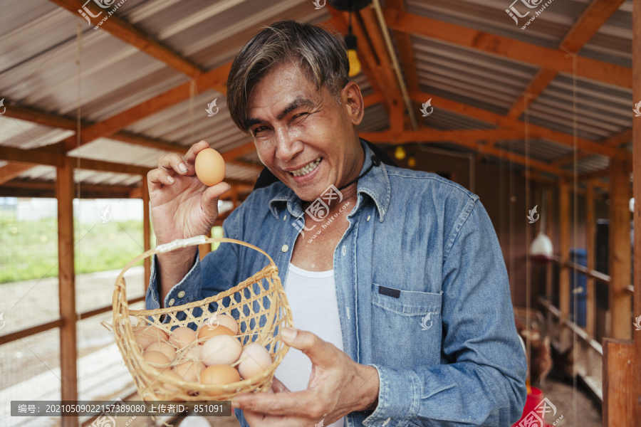 在养鸡场的房子里拿着鸡蛋篮子的亚洲老年农民。